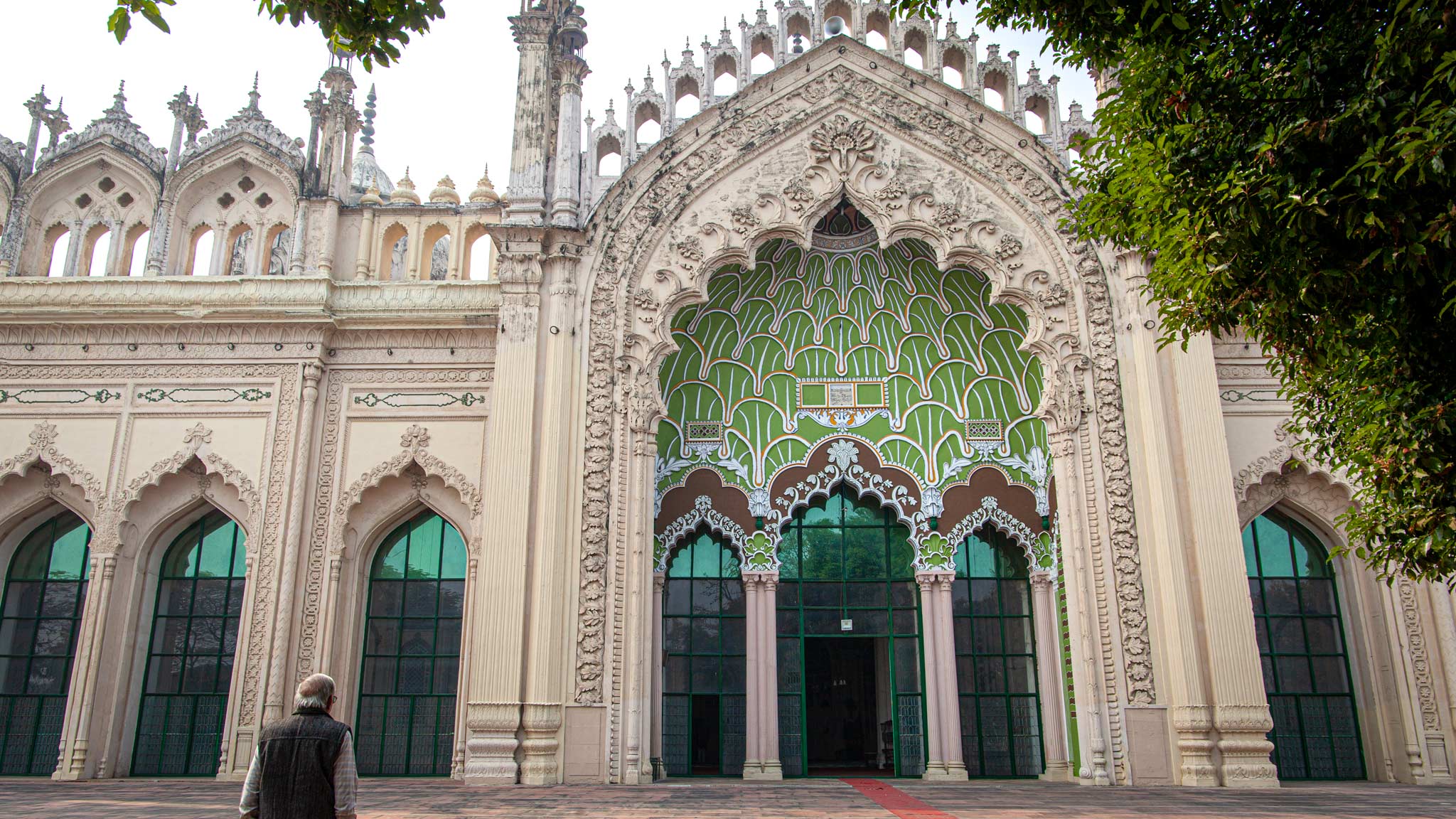 勒克瑙Jama Masjid清真寺的入口大门，一名男子站在左边祈祷，建筑上有各种彩色瓷砖的拱门