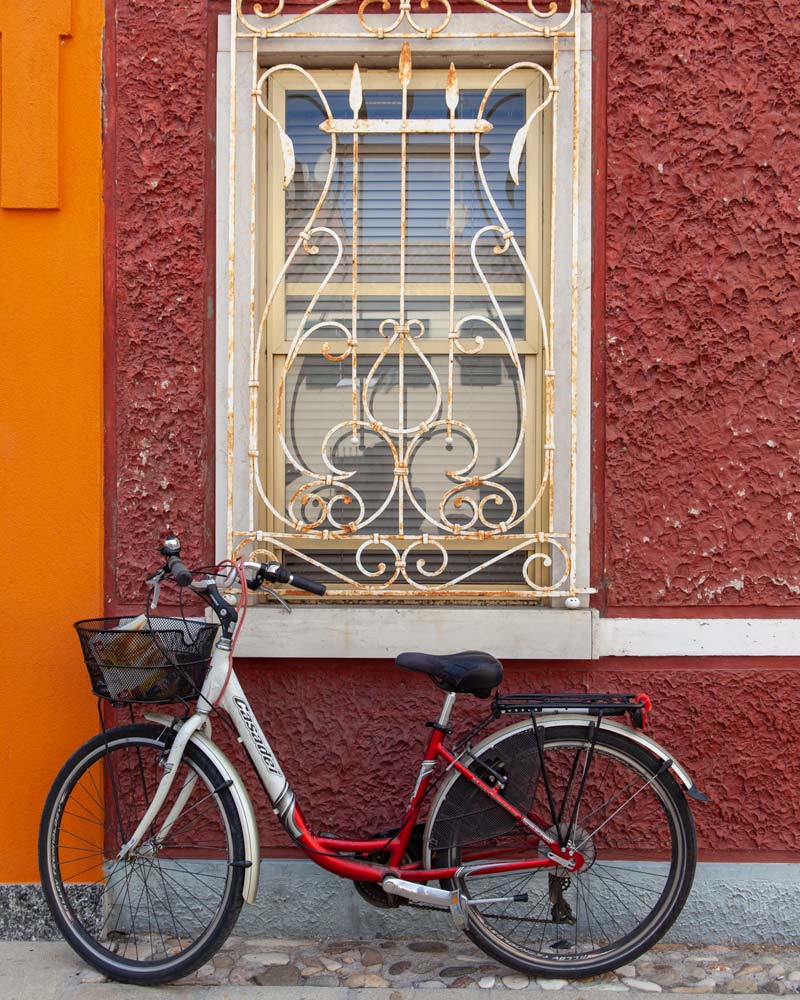 一辆红色的自行车靠在红色的墙上，上面有白色的铁架