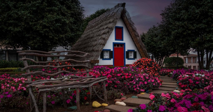 桑塔纳传统的茅草屋，一个尖尖的三角形房子，有彩色的蓝色和红色的窗户，外面有鲜花